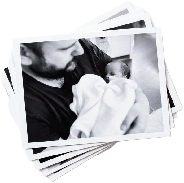 A pile of printed photographs, the top photo showing a father cradling his newborn baby